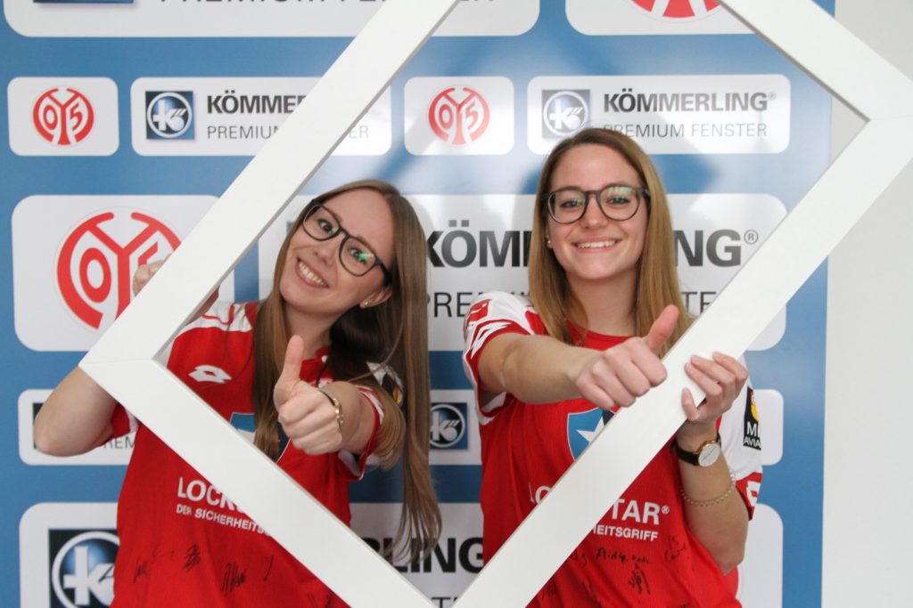 Zwei profine Studentinnen im Mainz 05 Trikot schauen durch ein Fensterprofil